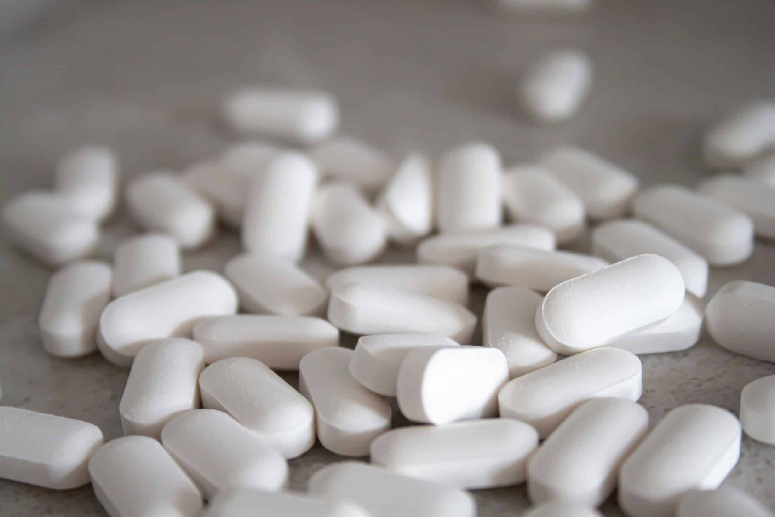 White chewable tablets on a gray surface, medication or supplement pills.