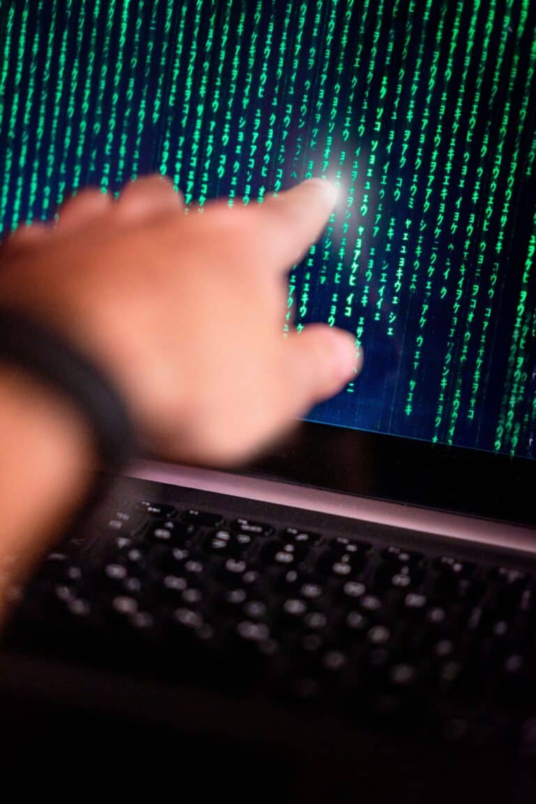 Hand pointing at digital code on laptop screen, emphasizing telehealth cybersecurity.