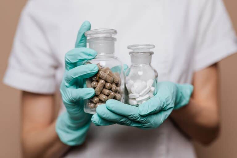 Medication bottles with pills and tablets in gloved hands for telehealth medication management.