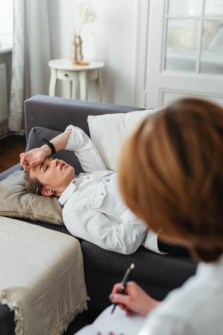 Woman lying on sofa during telehealth medical consultation at home.
