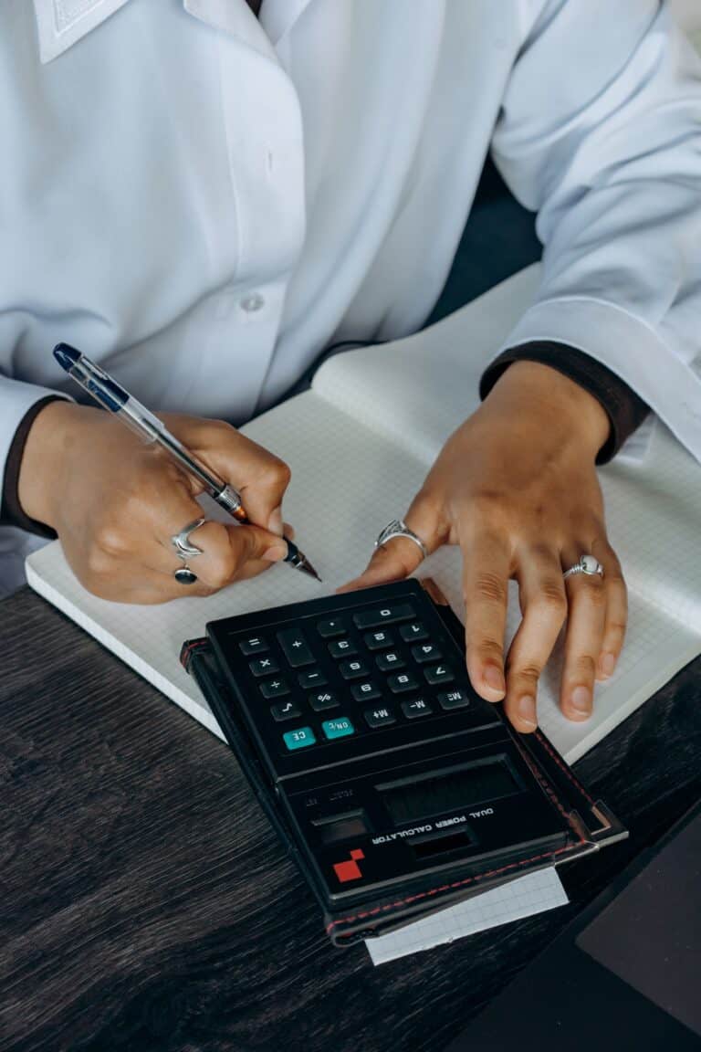 Healthcare professional using calculator and notebook for telehealth financial planning.